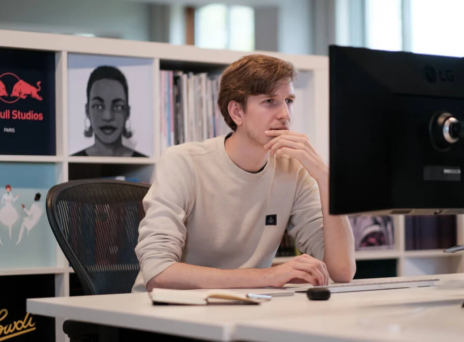  a young man sitting in front of a computer screen looking at his computer